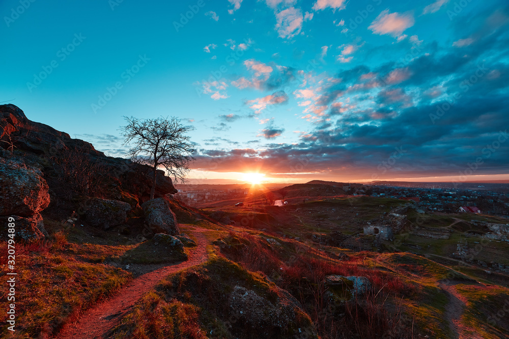view of the sunset in the clouds and the trail going away in the distance among the ruins of the fortress, stones and wood on the hill