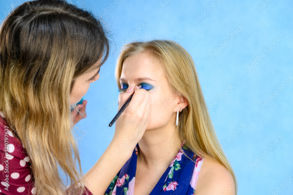 Beauty studio concept. Makeup artist applies makeup to a blonde woman model with long hair in an office. Photos in the beauty parlor.