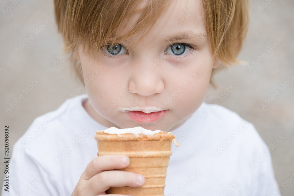 Beautiful baby with blue eyes in white tshirt is eating glass of white ice cream. Beautiful baby with blue eyes in white tshirt is eating glass of white ice cream.