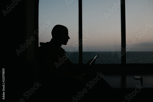 A stylish bald man sits with his smartphone aboard a ship. Silhouette portrait.