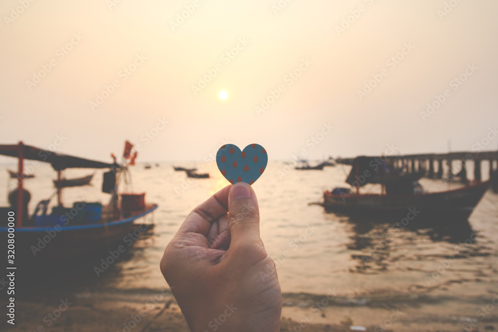 Close up of hand man holding a paper heart with the sea background in evening. love concept, happy valentine.