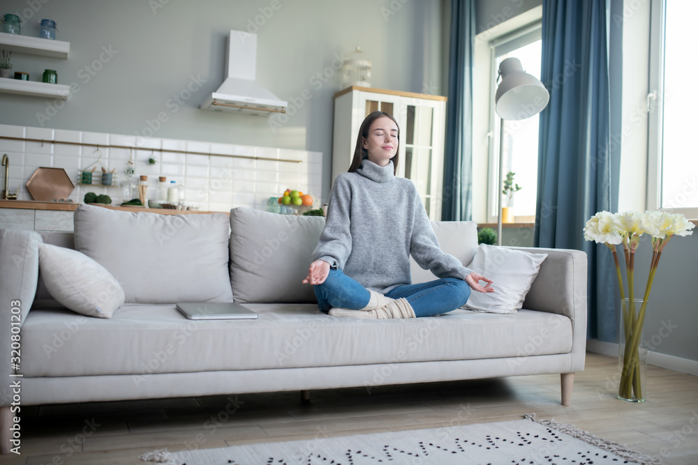 Young girl in a grey sweater meditating in a lotus pose Young girl in a grey sweater meditating in a lotus pose