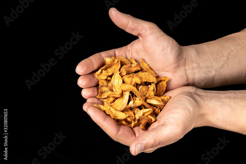 Tasty dried apple slices in male hands on black background