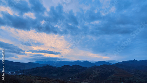 the sun setting behind the mountains in a cold and blue sky with clouds