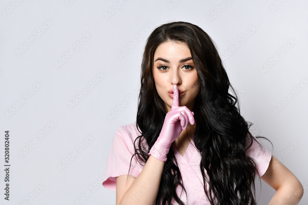 Young woman in pink uniform and disposable gloves posing isolated on white. She is showing a sign quiet. Copy space. Close up Young woman in pink uniform and disposable gloves posing isolated on white. She is showing a sign quiet. Copy space. Close up