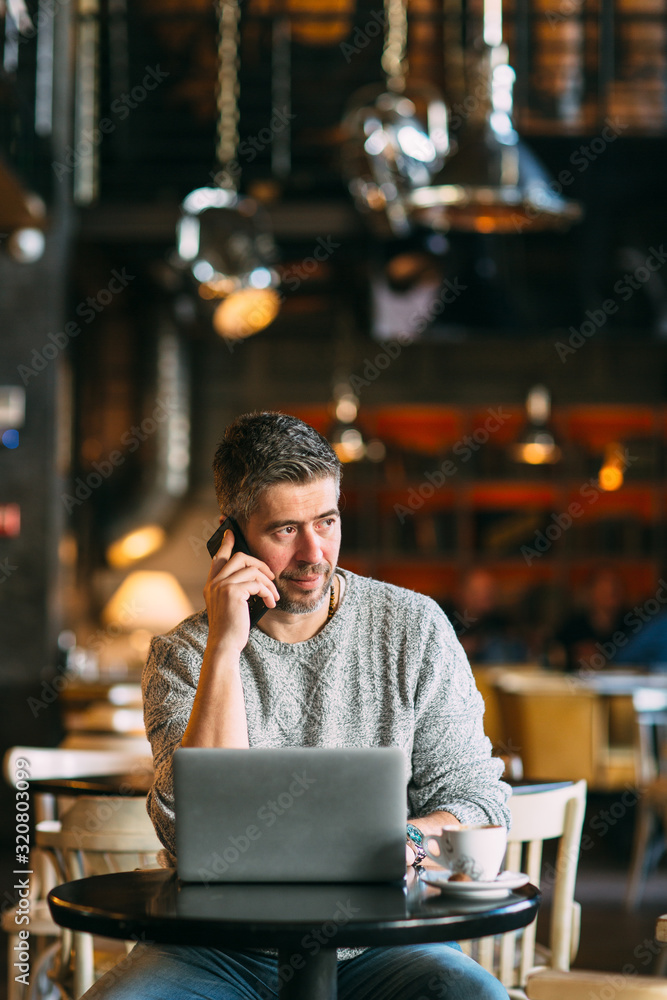 Middle-aged man working on a laptop computer, sitting at the cafeteria, lifestyle concept
