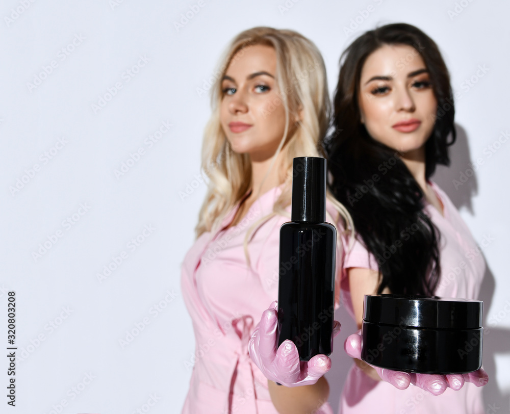 Two girls in pink suits posing isolated on white. Holding jar and bottle, cosmetic mockups for an advertising products. Close up Two girls in pink suits posing isolated on white. Holding jar and bottle, cosmetic mockups for an advertising products. Close up