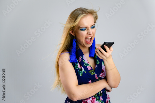 The model stands with the phone in her hands in various poses. Nice girl with fluttering hair and great make-up in front of the camera on a white background in a multi-colored dress.