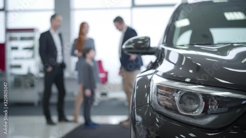 Wallpaper Mural Close-up of car headlamp with blurred people talking at the background. Caucasian dealer consulting family in car dealership. Auto industry, trading, purchasing. Torontodigital.ca