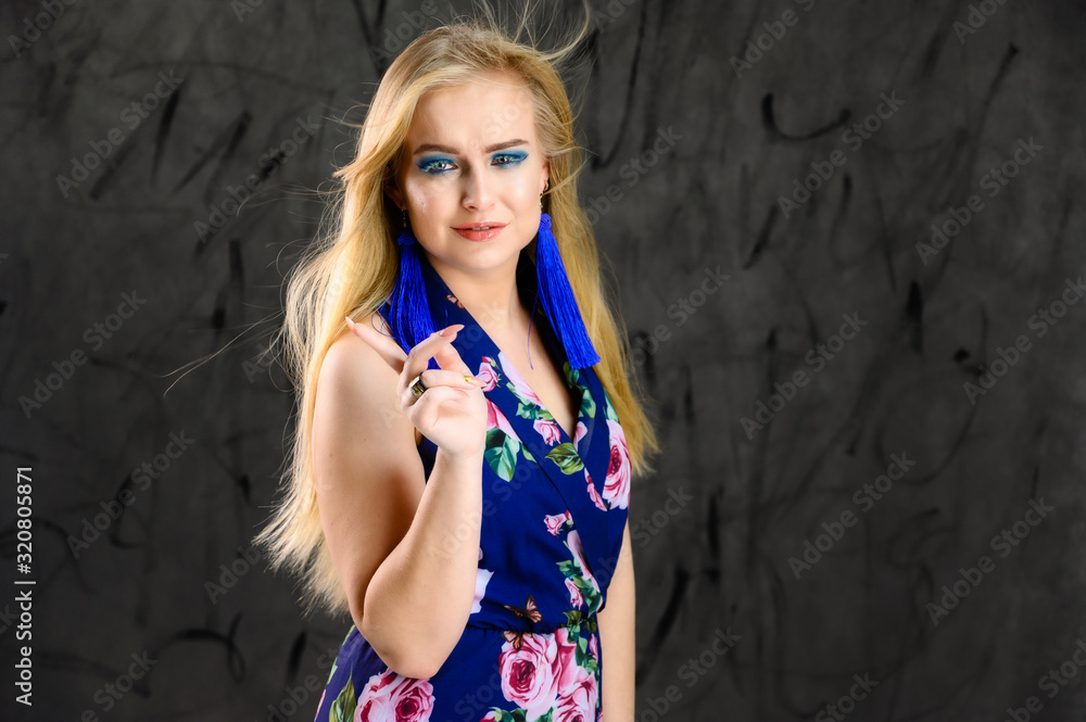 Fototapeta premium The model stands in different poses. Nice girl with flying hair and excellent make-up in front of the camera on a gray background in a multi-colored dress.