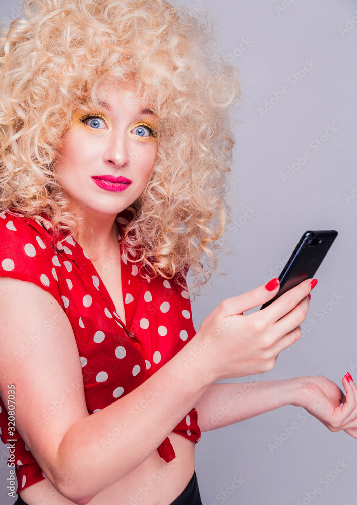 Beautiful blonde girl with a curly curly hairstyle, bright yellow make-up and red polka dot blouse looks at camera with pensive expression Beautiful blonde girl with a curly curly hairstyle, bright yellow make-up and red polka dot blouse looks at camera with pensive expression