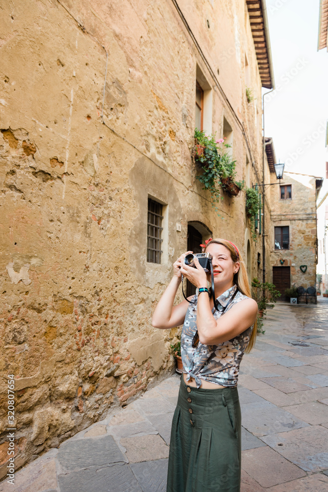 Young female traveler taking photo on a vintage camera in an old town of Montepulciano in Tuscany, Italy