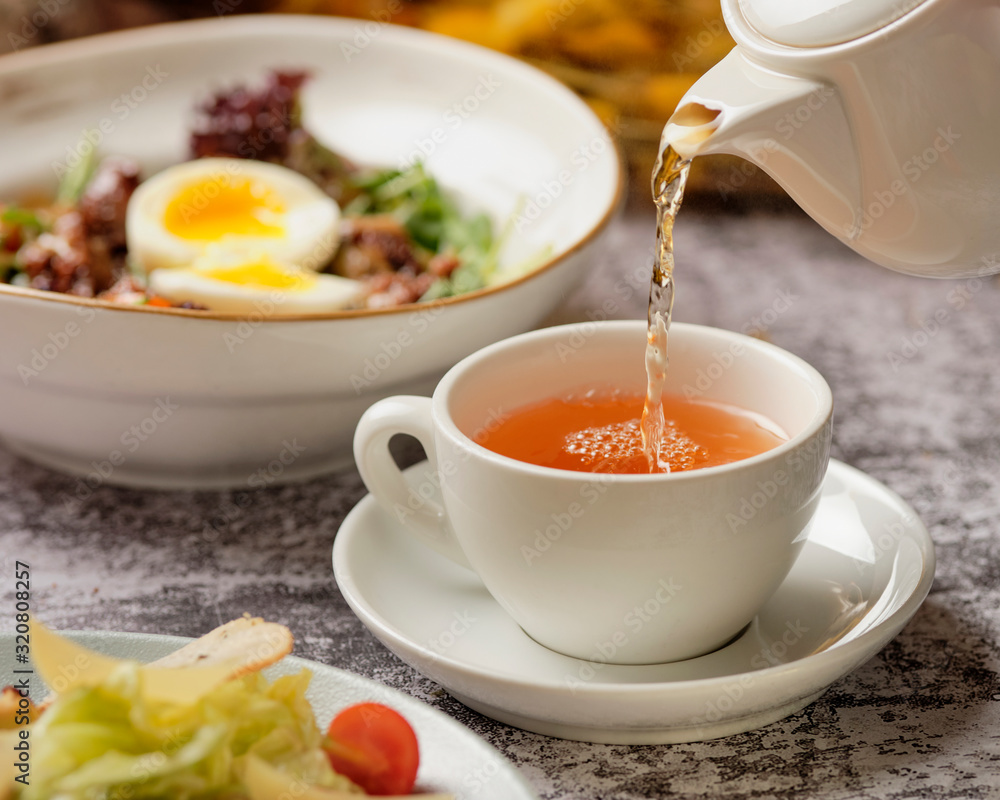 Tea being poured into tea cup. Cafe or bar table with dinner and tea. Communication concept. Restaurant background. Tea being poured into tea cup. Cafe or bar table with dinner and tea. Communication concept. Restaurant background.