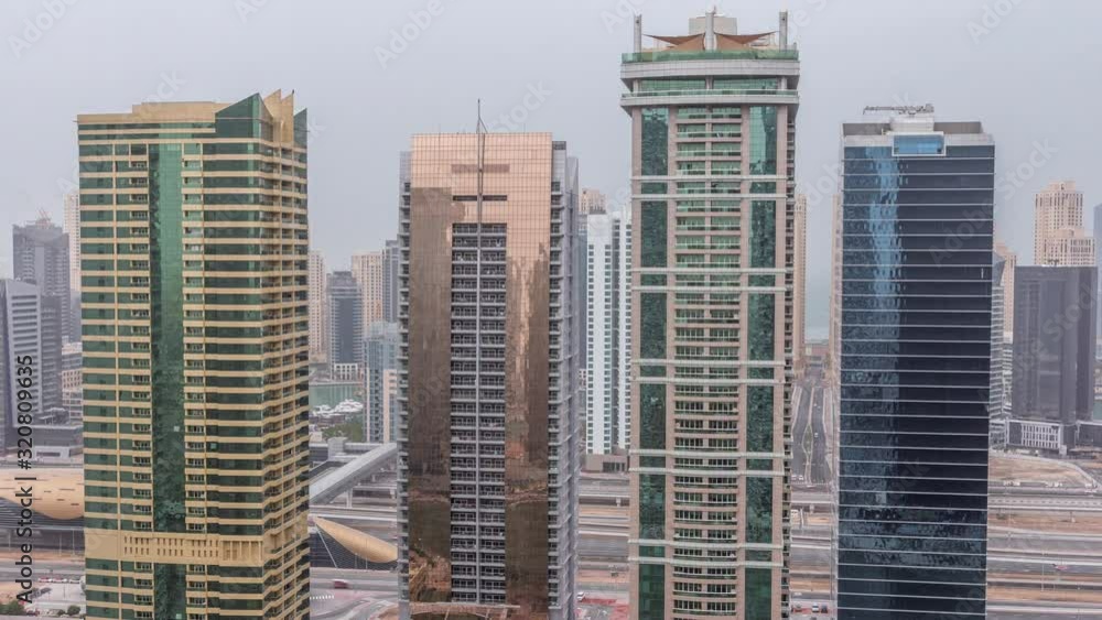 Residential and office buildings in Jumeirah lake towers district night to day transition timelapse before sunrise in Dubai. Aerial panoramic view from above with illuminated modern skyscrapers Residential and office buildings in Jumeirah lake towers district night to day transition timelapse before sunrise in Dubai. Aerial panoramic view from above with illuminated modern skyscrapers