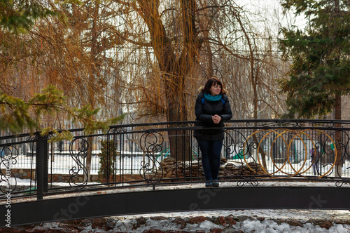 A young girl stands on a bridge in a city park on a weekend, sunny spring day. She enjoys the awakening of nature after winter and the warm sun. Early spring in the city.