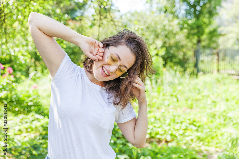 Beautiful young brunete woman with brown hair in trendy yellow sunglasses resting and smiling on park or garden green background. European woman. Portrait of happy teenage girl relaxing outdoor. Beautiful young brunete woman with brown hair in trendy yellow sunglasses resting and smiling on park or garden green background. European woman. Portrait of happy teenage girl relaxing outdoor.