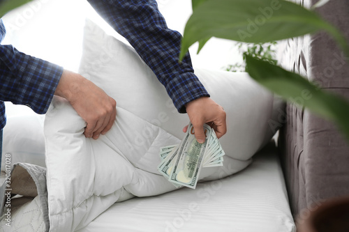 Man hiding dollar banknotes under blanket in bedroom  closeup. Money savings