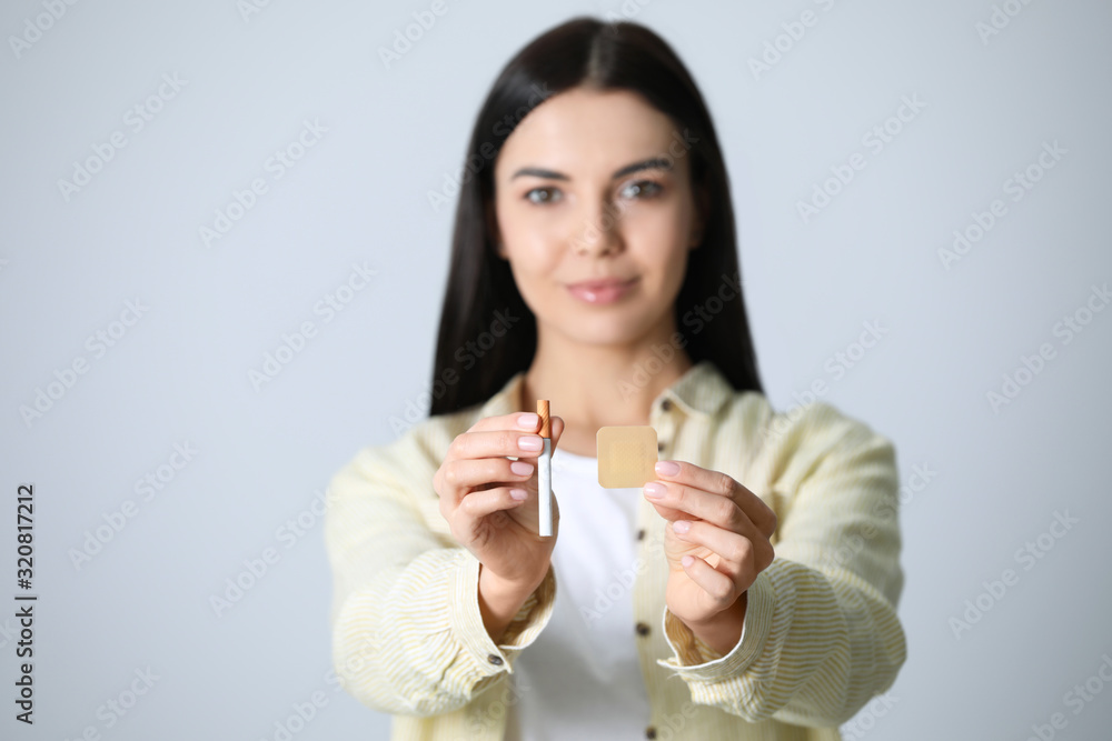 Happy young woman with nicotine patch and cigarette against light grey background, focus on hands Happy young woman with nicotine patch and cigarette against light grey background, focus on hands