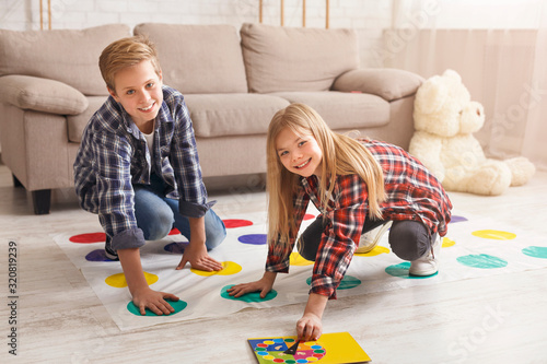 Cheerful siblings playing twister game on floor having fun indoor