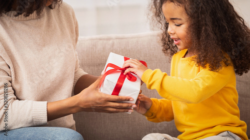 Little Girl Receiving Gift From Mother Sitting On Couch Indoor