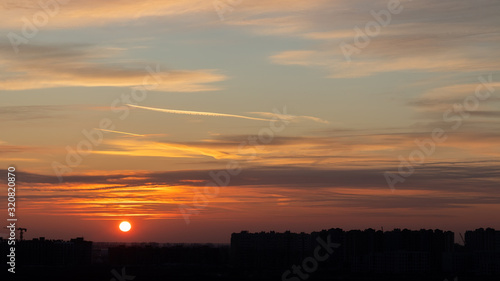 Beautiful dramatic sunset background. Orange sky with sun, clouds and black silhouettes of urban buildings