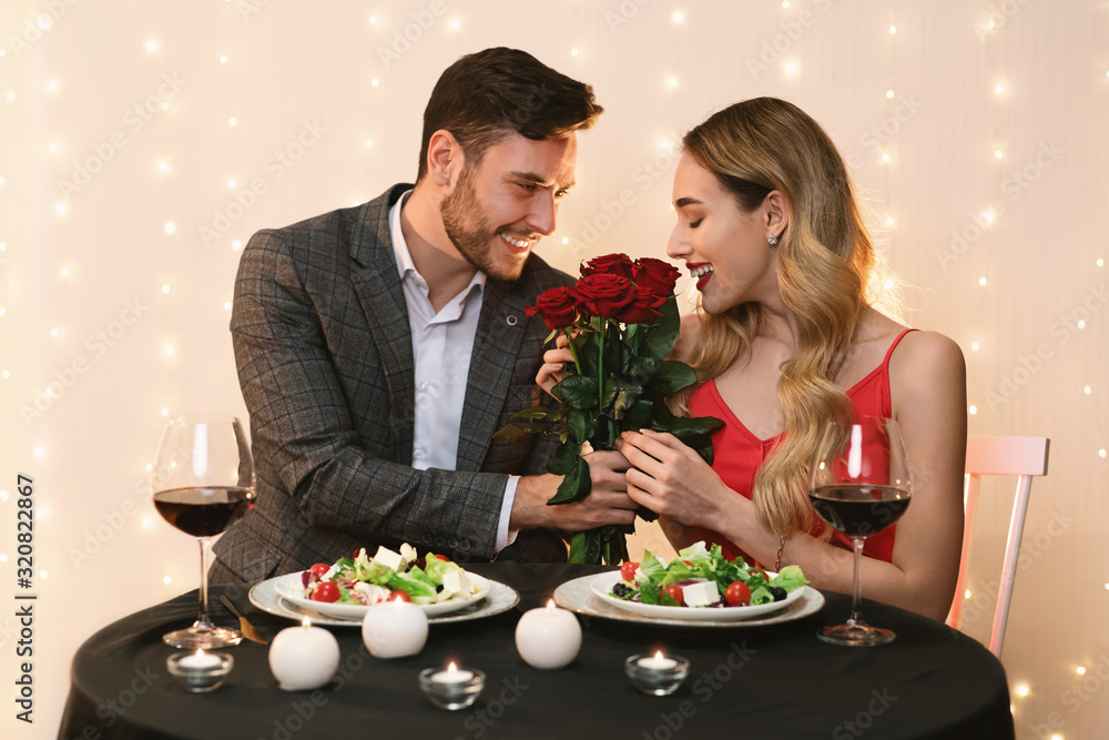 Handsome Man Presenting Roses To Happy Girlfriend On Date In Restaurant Handsome Man Presenting Roses To Happy Girlfriend On Date In Restaurant