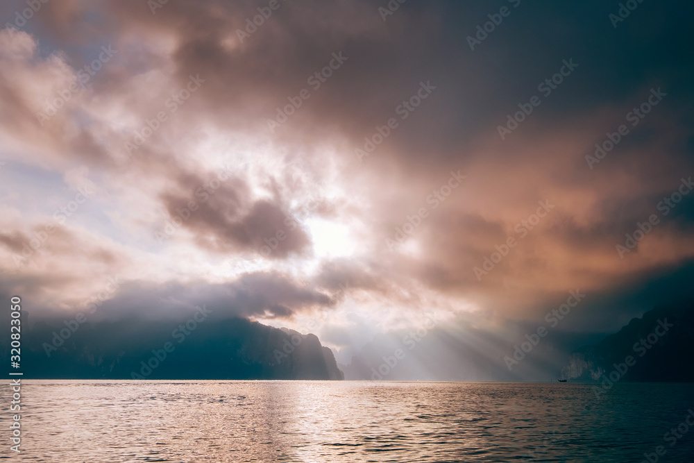 Cheow Lan Lake in the early morning under sunrise rays struggle through the storm clouds , Khao Sok national park, Thailand