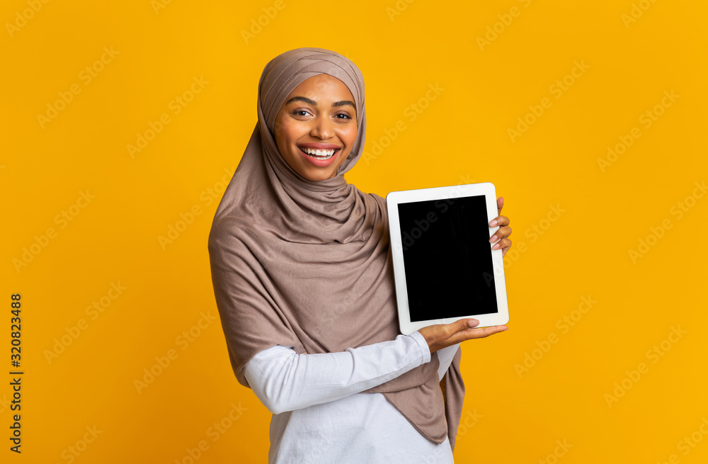 Cheerful afro girl in headscarf presenting digital tablet with black screen Cheerful afro girl in headscarf presenting digital tablet with black screen