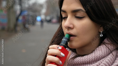 Cool portrait of vaping young woman on the street in a winter day. Camera follows her hand movement with electronic vape-device
