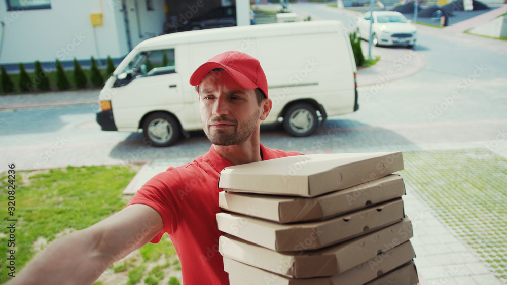 Scene from a house spyhole. Handsome delivery man with pizza boxes and cash machine approaching to customer door ringing on the bell waiting outdoors. Delivery services. Modern city. Scene from a house spyhole. Handsome delivery man with pizza boxes and cash machine approaching to customer door ringing on the bell waiting outdoors. Delivery services. Modern city.
