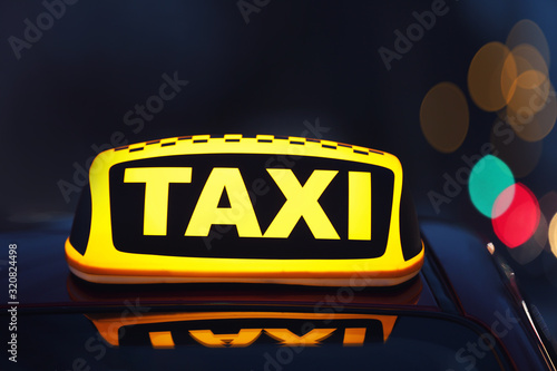 Taxi car with yellow roof sign on city street in evening, closeup