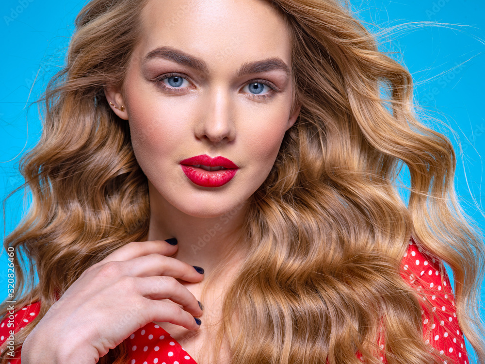 Fototapeta premium Portrait of a beautiful young blonde. Beautiful girl with long white hair. Face close-up of a sexy girl. Model in a red shirt poses in the Studio. Caucasian woman with red lipstick on her lips.