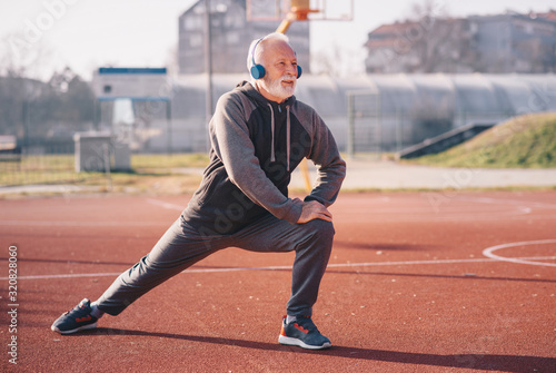 An older man stretching his legs at the basketball court wearing headphones.sportsperson