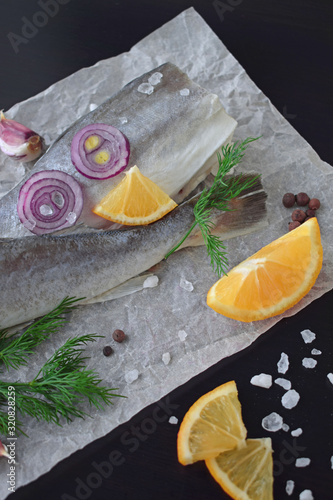 Fresh sea fish with herbs, spices and lemon on a black background.