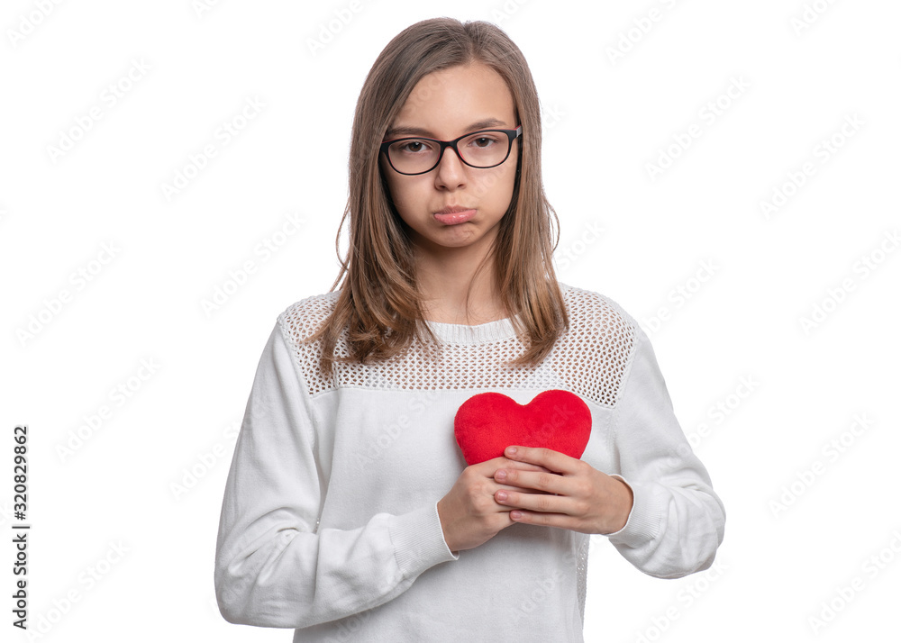 UnHappy Valentines Day. Cute upset Teen Girl with Eyeglasses in Love with Red plush Heart in her hands. Sad Child, isolated on white background. UnHappy Valentines Day. Cute upset Teen Girl with Eyeglasses in Love with Red plush Heart in her hands. Sad Child, isolated on white background.