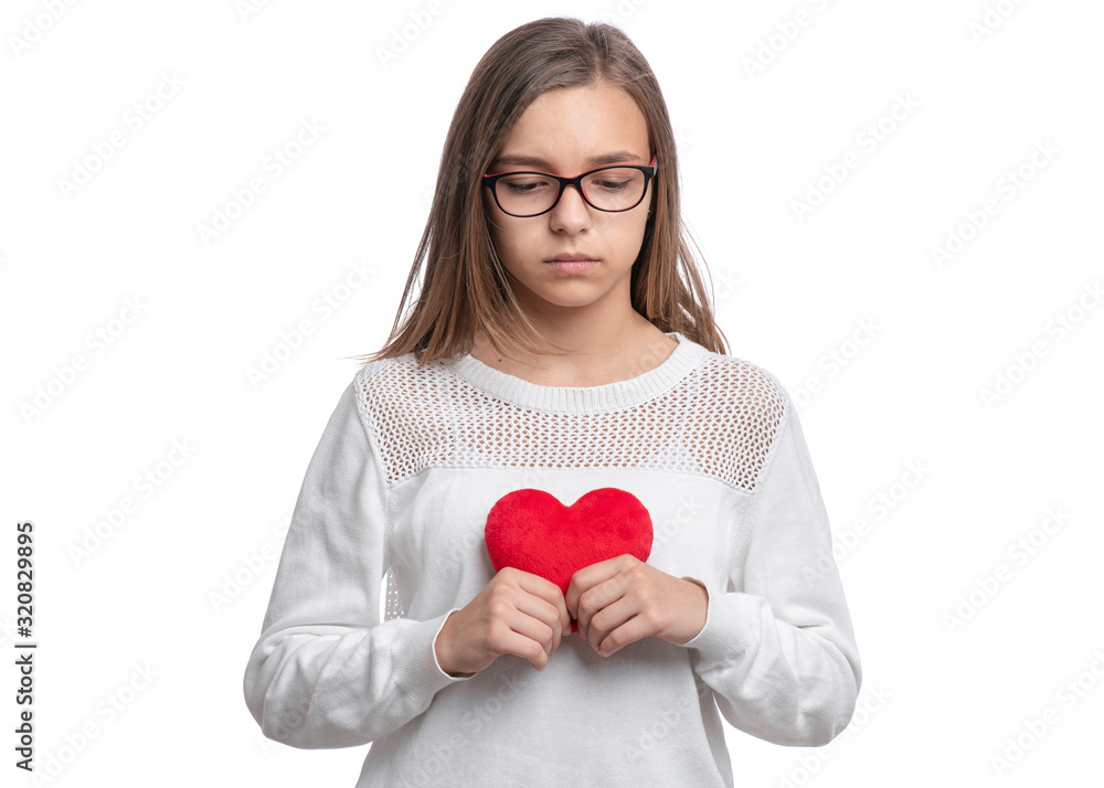 UnHappy Valentines Day. Cute upset Teen Girl with Eyeglasses in Love with Red plush Heart in her hands. Sad Child, isolated on white background. UnHappy Valentines Day. Cute upset Teen Girl with Eyeglasses in Love with Red plush Heart in her hands. Sad Child, isolated on white background.