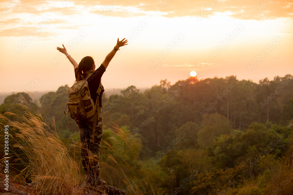 Asian traveler woman with backpack standing hands up enjoying sunset on peak mountain at natural park Asian traveler woman with backpack standing hands up enjoying sunset on peak mountain at natural park