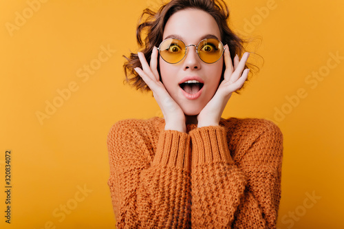 Excited young woman in round yellow glasses posing on bright background. Studio shot of beautiful caucasian girl in vintage accessories.