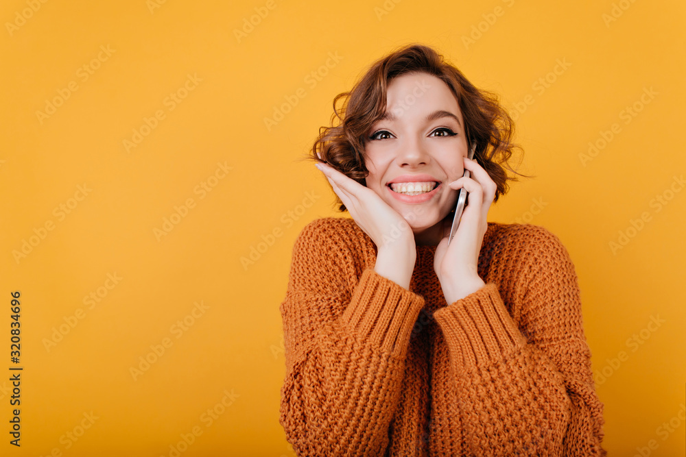 Close-up portrait of blissful white girl in trendy woolen sweater. Indoor photo of refined caucasian female model in bright knitted attire isolated on yellow background. Close-up portrait of blissful white girl in trendy woolen sweater. Indoor photo of refined caucasian female model in bright knitted attire isolated on yellow background.