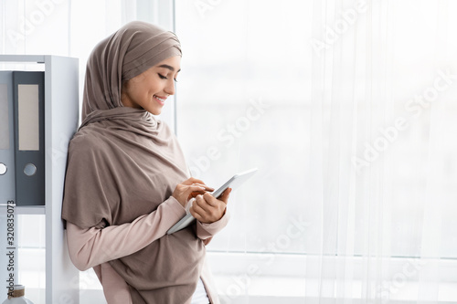 Smiling Arabic Secretary Using Digital Tablet While Standing Near Office Window