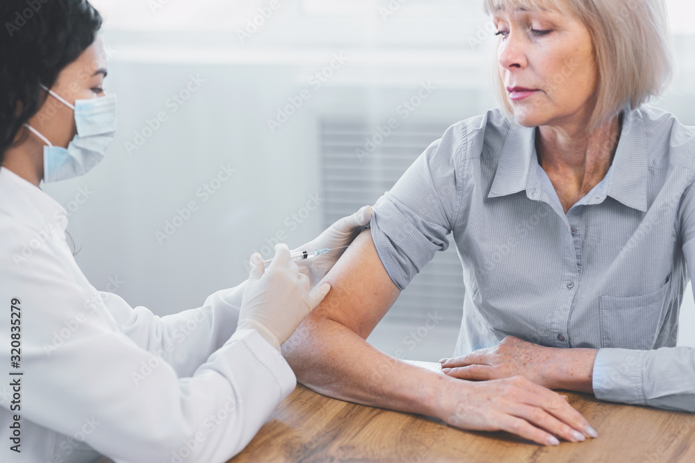Fototapeta premium Latina doctor doing vaccination to elderly woman