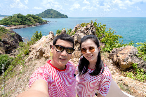 Happy traveling couple taking selfie on the mountain against the ocean.