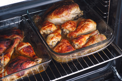 Roasted chicken legs and breasts in glass baking trays in an oven
