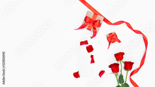 Red roses, silver blank mockup, red ribbon, craft paper gift, petals isolated on white backdrop. Copy space. Romantic festive template concept for greeting card, advertising, Women’s day, Mother's Day