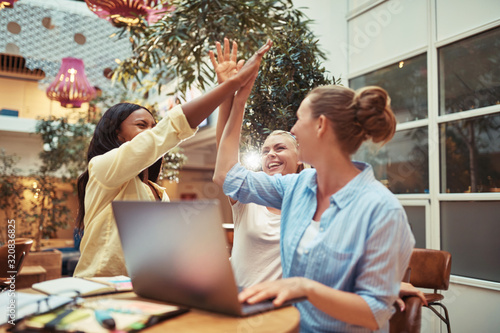 Diverse businesswomen laughing and high fiving in an office loun photo