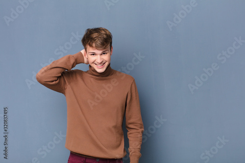 young blonde man laughing cheerfully and confidently with a casual, happy, friendly smile isolated against flat wall photo