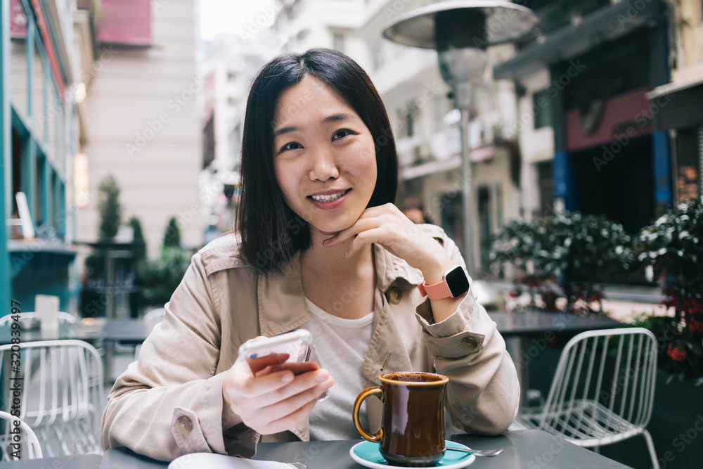 Smiling Asian woman using smartphone in cafe