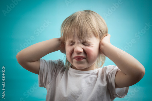 child does not hear well after otitis media. the child's ears hurt. the girl covered her ears with her hands photo