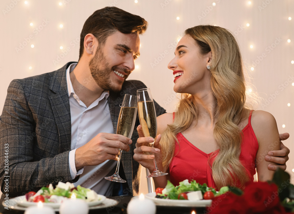 Young Couple Having Romantic Evening In Restaurant, Clinking Glasses With Champagne Young Couple Having Romantic Evening In Restaurant, Clinking Glasses With Champagne
