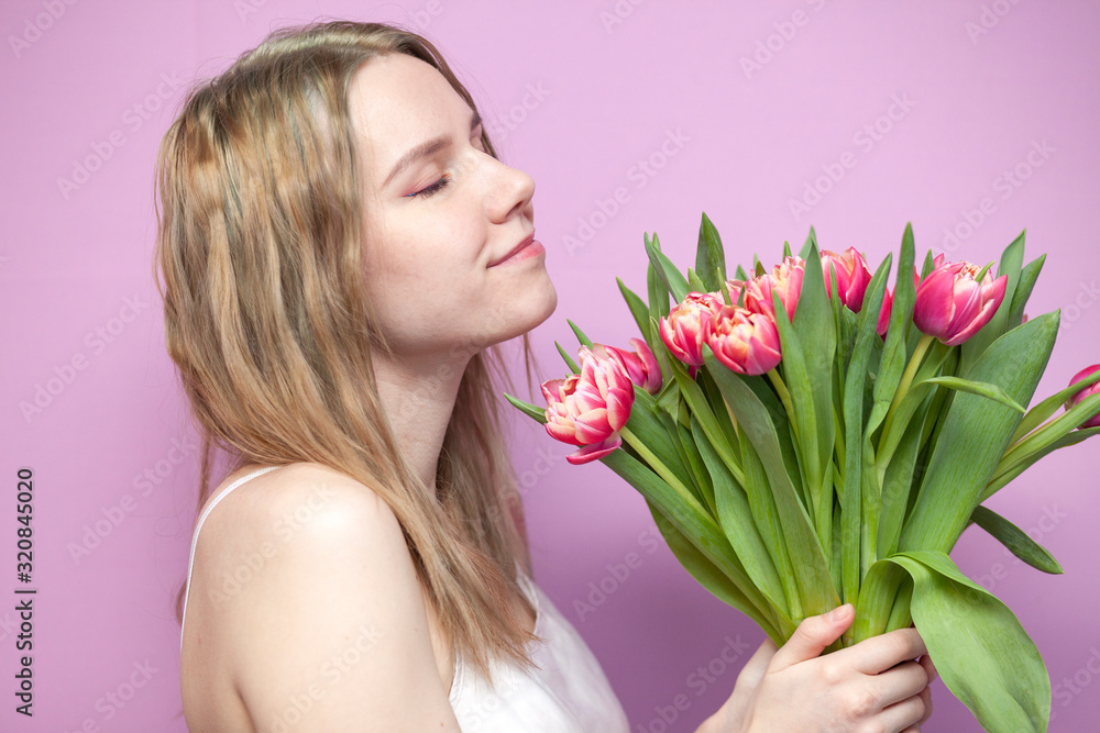 young beautiful girl with a bouquet of flowers on a colored pink background, a woman holds tulips and smiles young beautiful girl with a bouquet of flowers on a colored pink background, a woman holds tulips and smiles